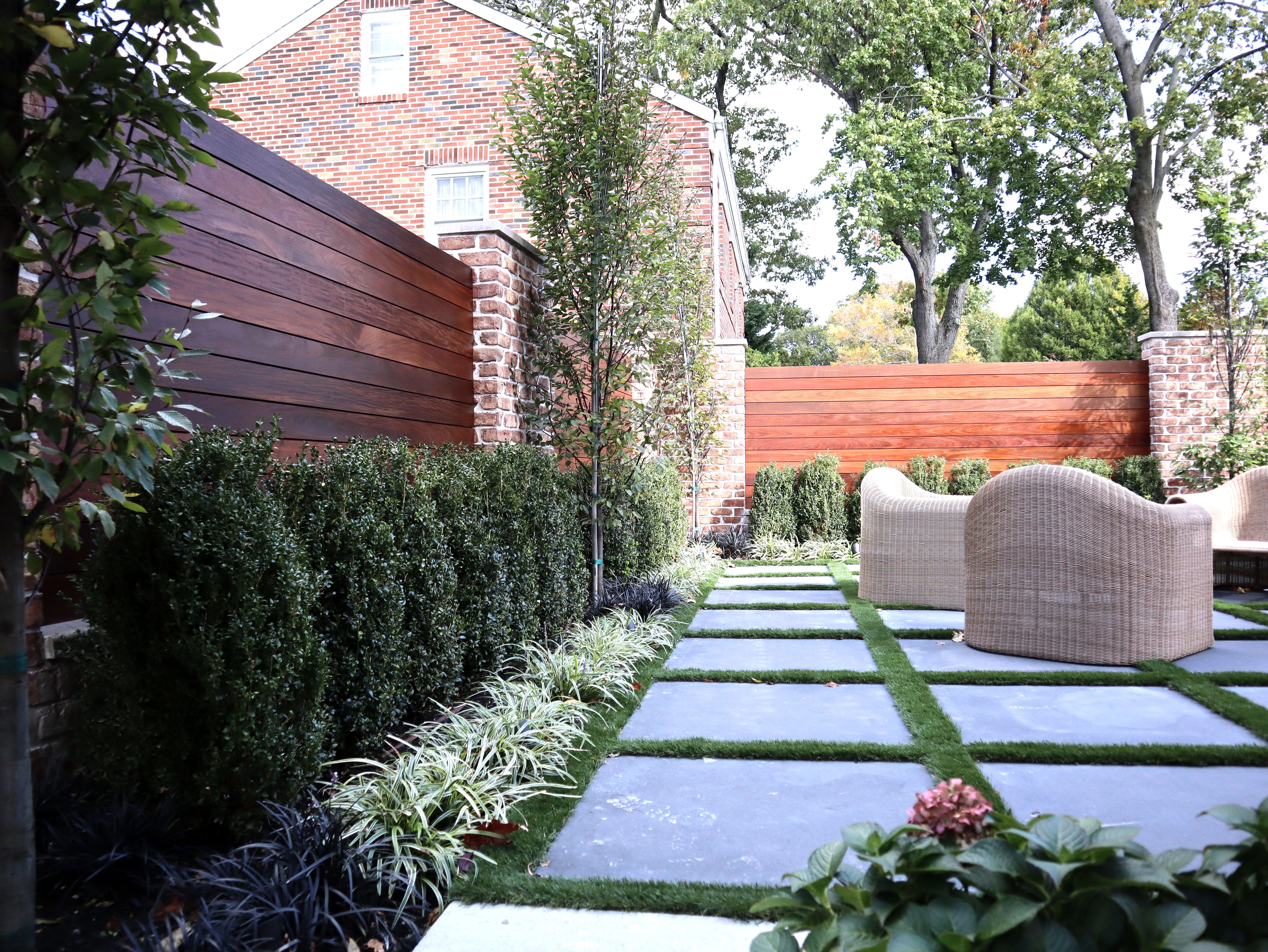 Backyard with bluestone pavers in turf, wood fence, brick wall, hedges